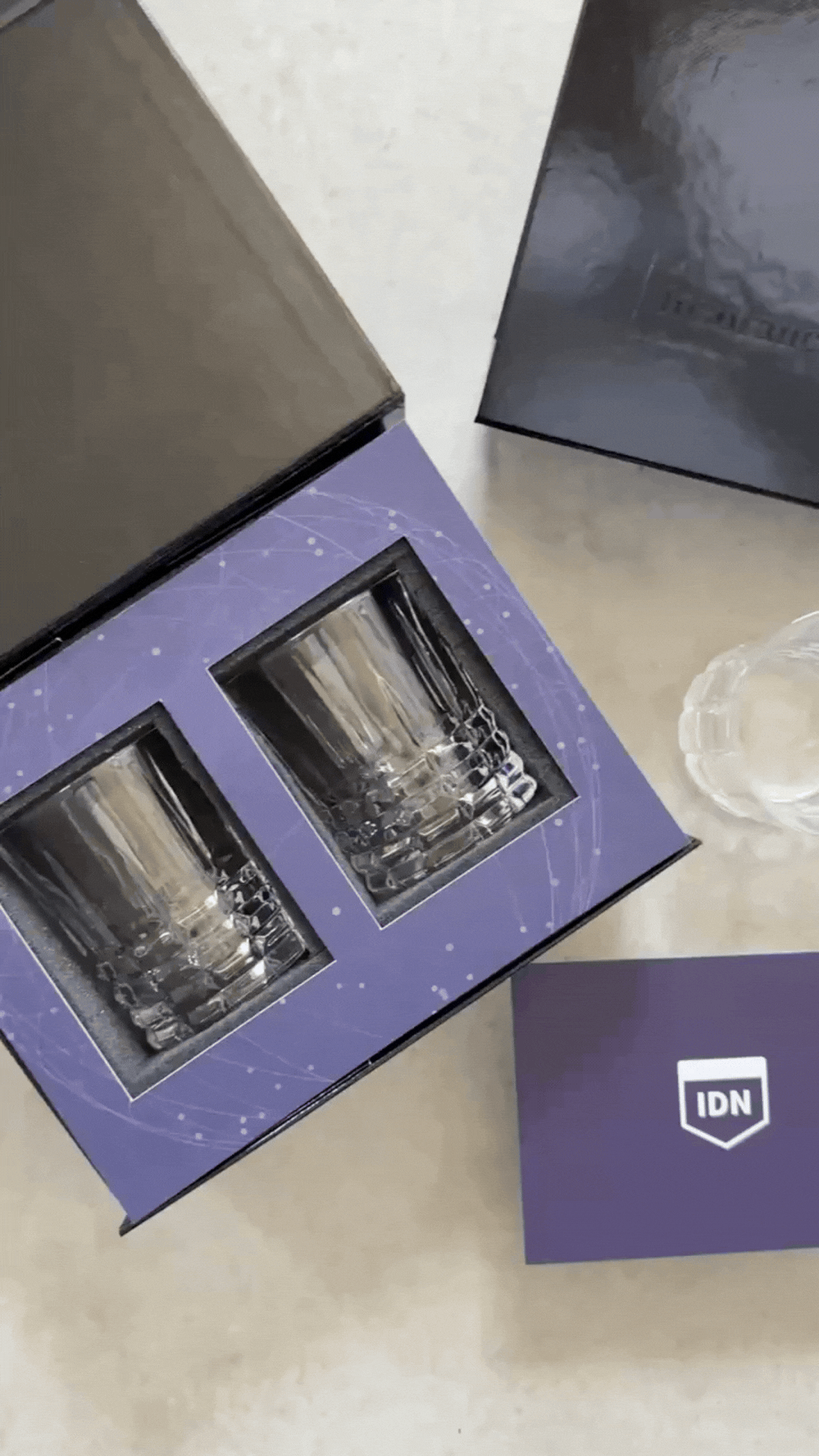 An open professional gift box with two branded crystal glasses in foam, an embossed lid and a matching insert card