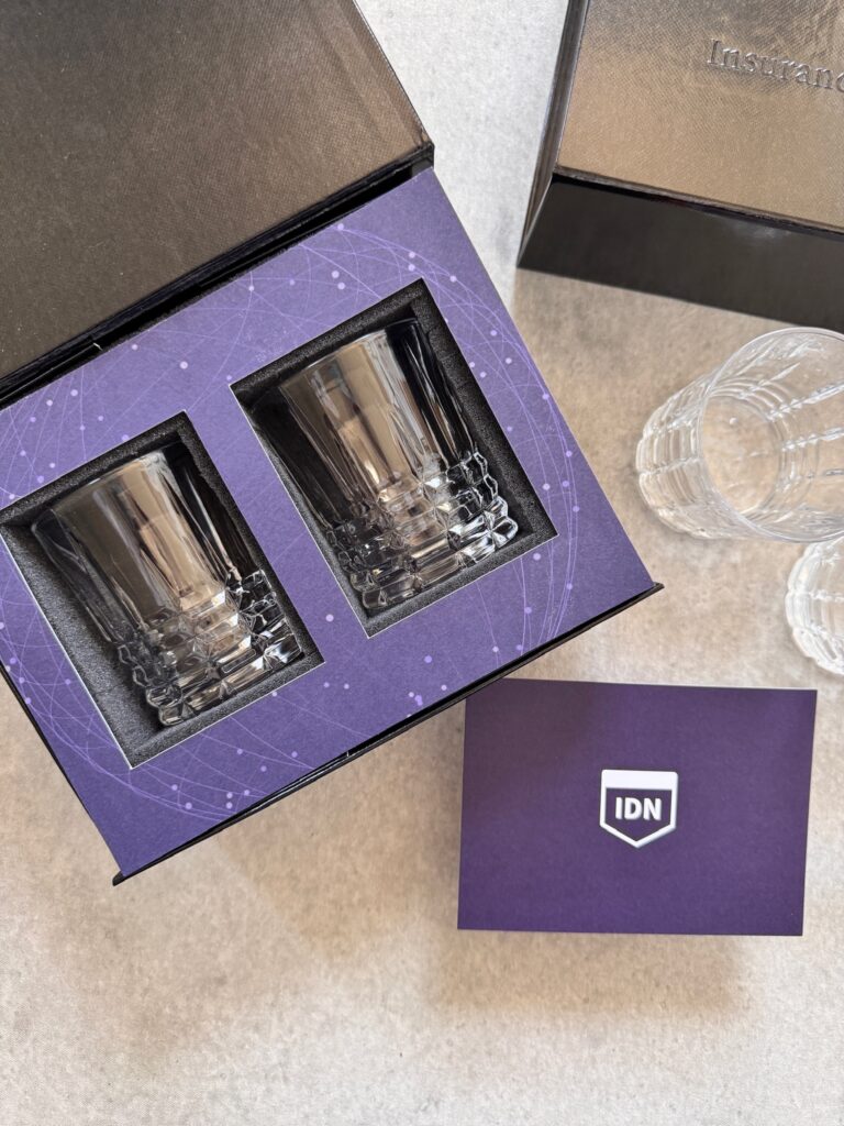 An open professional gift box with two branded crystal glasses in foam, an embossed lid and a matching insert card