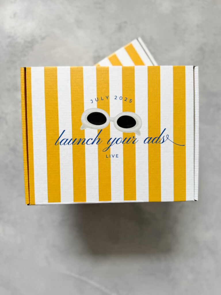 Close-up of a yellow striped events gifting box featuring sunglasses graphic and "Launch Your Ads Live July 2025" branding.
