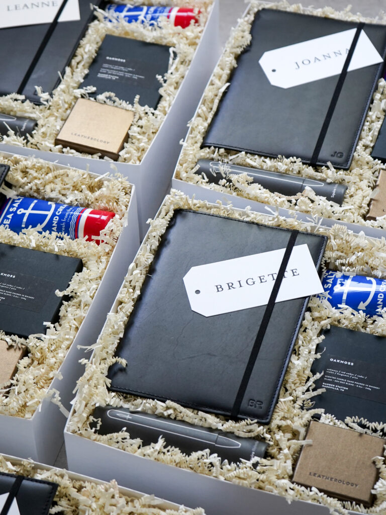 Virtual event gifts featuring personalized leather padfolios, name tags, and Leatherology packaging arranged for individual recipients including Brigette and Joanna