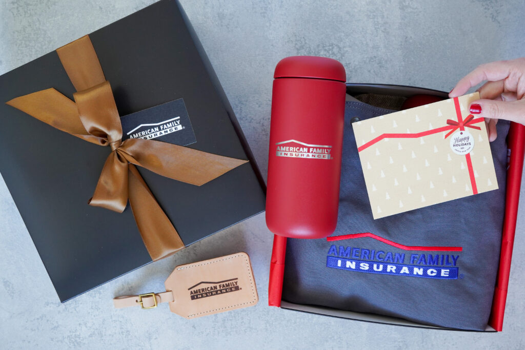 Corporate Christmas gift box with branded travel tumbler, tote bag, and leather luggage tag tied with a satin bow