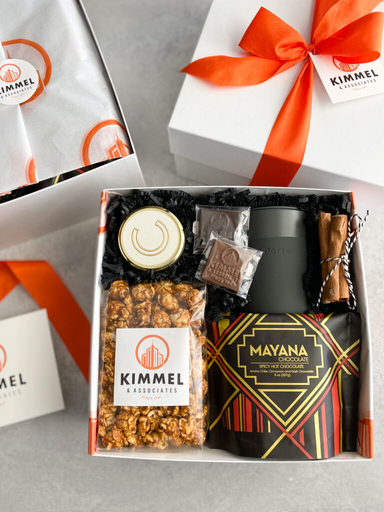 Corporate Christmas gift box with caramel popcorn, hot chocolate, branded chocolates, and travel mug tied with orange ribbon