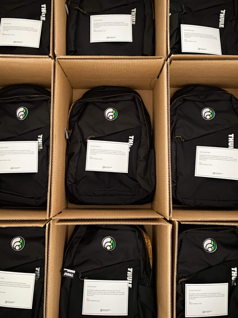 Rows of employee onboarding gift boxes with branded backpacks and personalized thank-you cards ready for bulk shipping